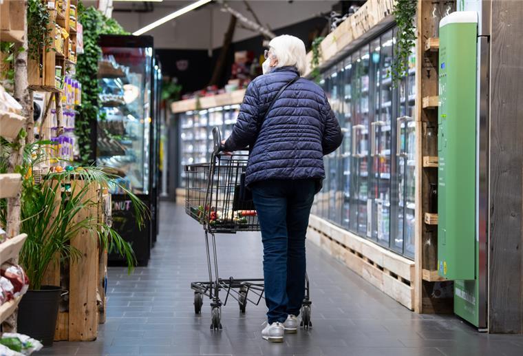 Eine Frau läuft mit ihrem Einkaufswagen durch einen Supermarkt. 