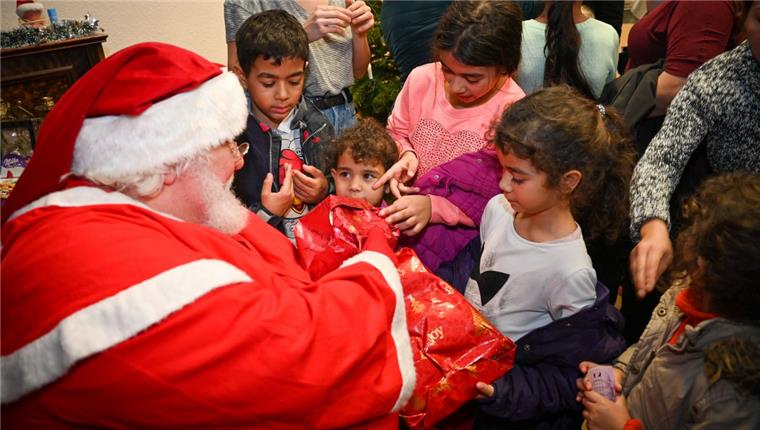 Hier werden Wünsche von bedürftigen Kindern aus Bremerhaven erfüllt Ein Mann in Weihnachtsmann-Kostüm sitzt vor einer Schar Kinder und überreicht Geschenke.