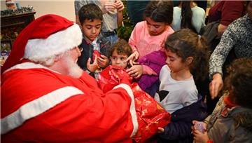 Ein Mann in Weihnachtsmann-Kostüm sitzt vor einer Schar Kinder und überreicht Geschenke.