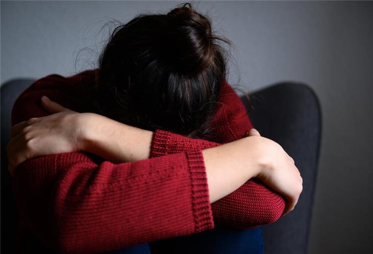 Winterblues oder Depression? - Wo liegt der Unterschied Eine Frau sitzt mit dem Kopf in den Armen versunken auf einem Stuhl.
