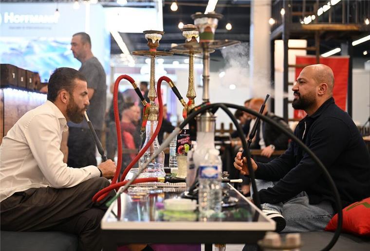 Besucher der Fachmesse Intertabac sitzen an einem Tisch und inhalieren Dampf aus Wasserpfeifen (Shishas).
