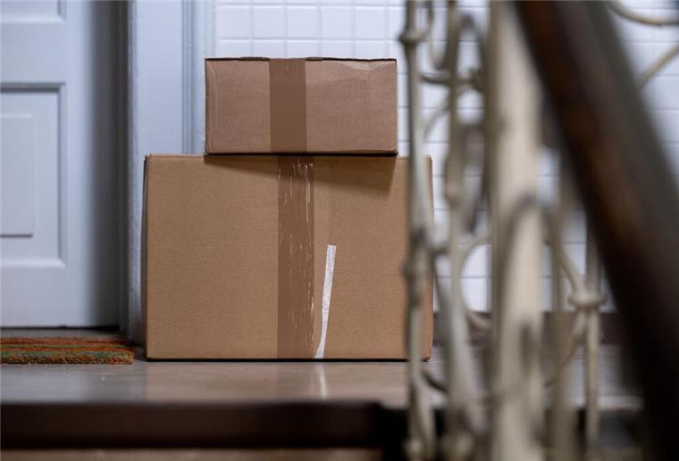Zwei Pakete liegen in einem Mehrfamilienhaus im Treppenhaus vor einer Wohungstür.