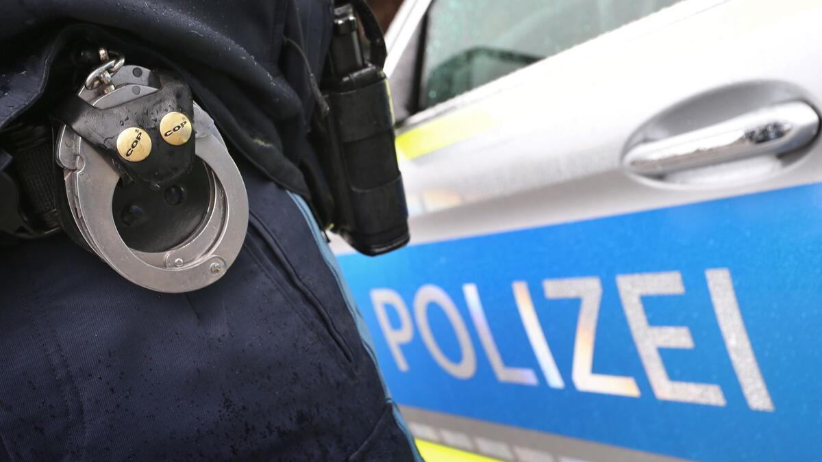 Räuberische Diebstähle in Bremerhaven: Polizei ermittelt und sucht Zeugen Ein Polizist mit Handschellen und einer Pistole am Gürtel steht vor einem Streifenwagen.