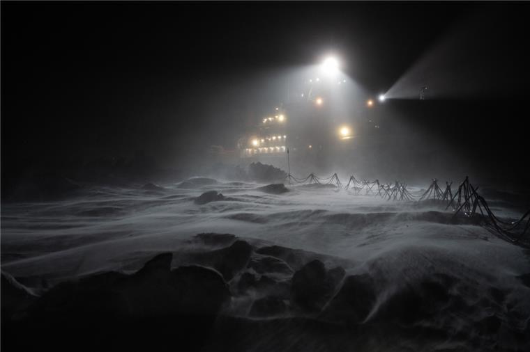 Ein großen Schiff ist in der Nacht hell erleuchtet - ringsherum liegt Schnee und Eis.