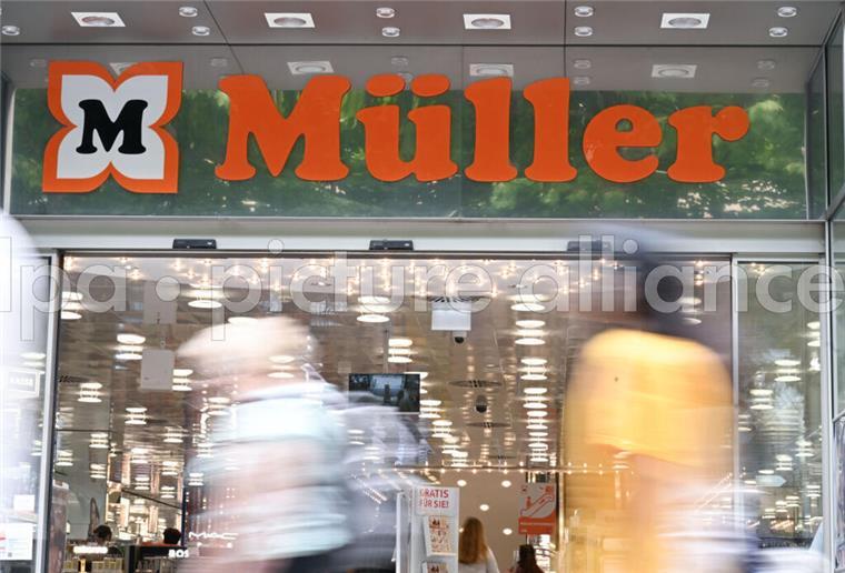 Das Logo der Drogeriemarktkette Müller ist am Eingang einer Filiale angebracht. Im Vordergrund laufen Passanten vorbei