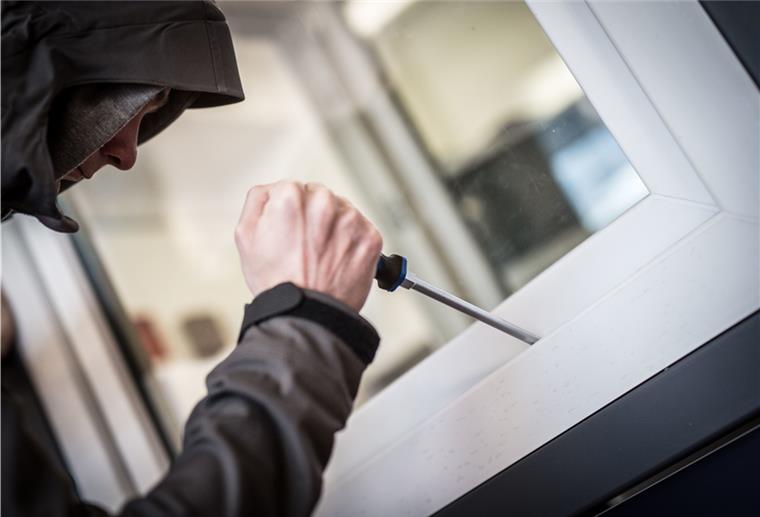 Ein Einbrecher öffnet mit einem Schraubenzieher ein Fenster. 