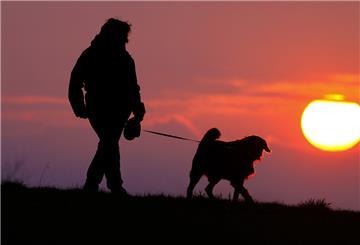 Eine Frau geht am Morgen, kurz nach Sonnenaufgang, mit ihrem Hund spazieren.