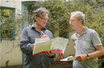 Zwei Männer stehen vor einem Haus. der eine (der Berater) trägt Dinge in eine Mappe mit der Beschriftung "Dämmvisite" ein, der andere schaut aufmerksam zu.