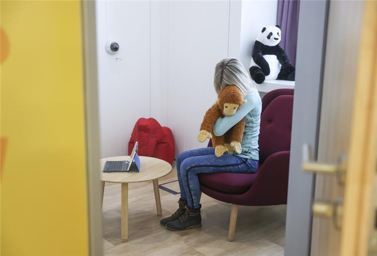 Ein Kind sitzt in einem Gesprächszimmer und umklammert ein Plüschtier. 