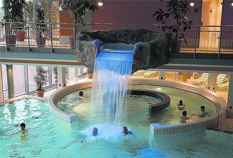 Besucher der Moor-Therme schwimmen im Wasser und stehen unter einem Wasserfall.