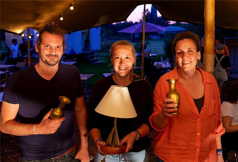 Welche Events erwarten euch im Juli im Beet und was geht beim Kneipenquiz ab? Ein Mann und zwei Frauen halten Preise hoch
