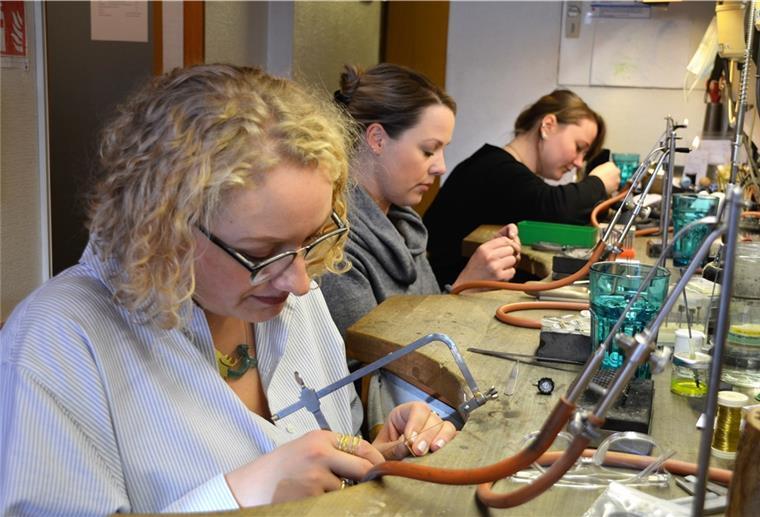 Handwerk und Kunst liegen eng beieinander Die Goldschmiedinnen sind in ihrer Schmiedewerkstatt und bearbeiten mit Gerätschaften den Schmuck.