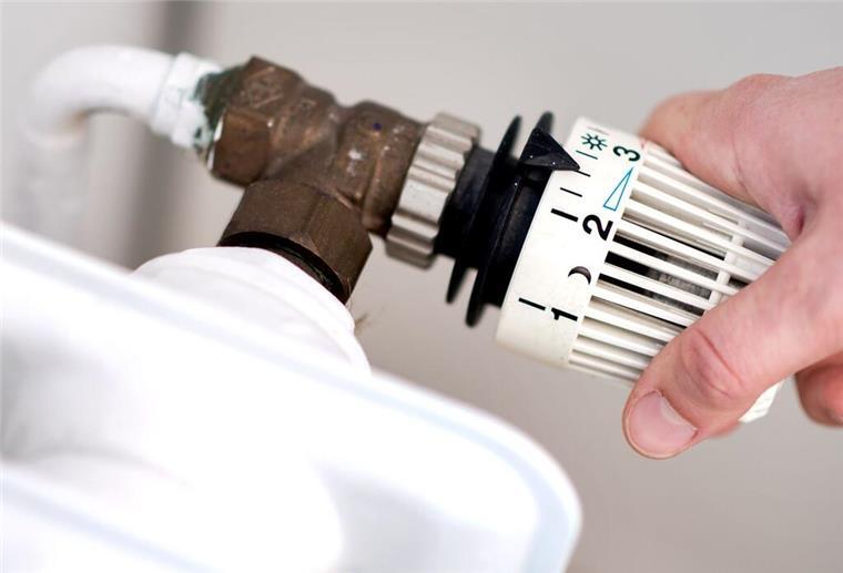 Eine Frau dreht am Thermostat eines Heizkörpers.