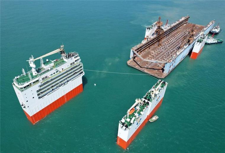 Marodes Ölschiff reist zum Verschrotten extra nach Europa - Aktion sorgt für Ärger Das halbtauchfähige Schwerlastschiff „Hua Rui Long“ bei geöffneter Deckstruktur auf See, bereit zur Aufnahme eines großen Objekts; mehrere Schlepper unterstützen das Manöver.