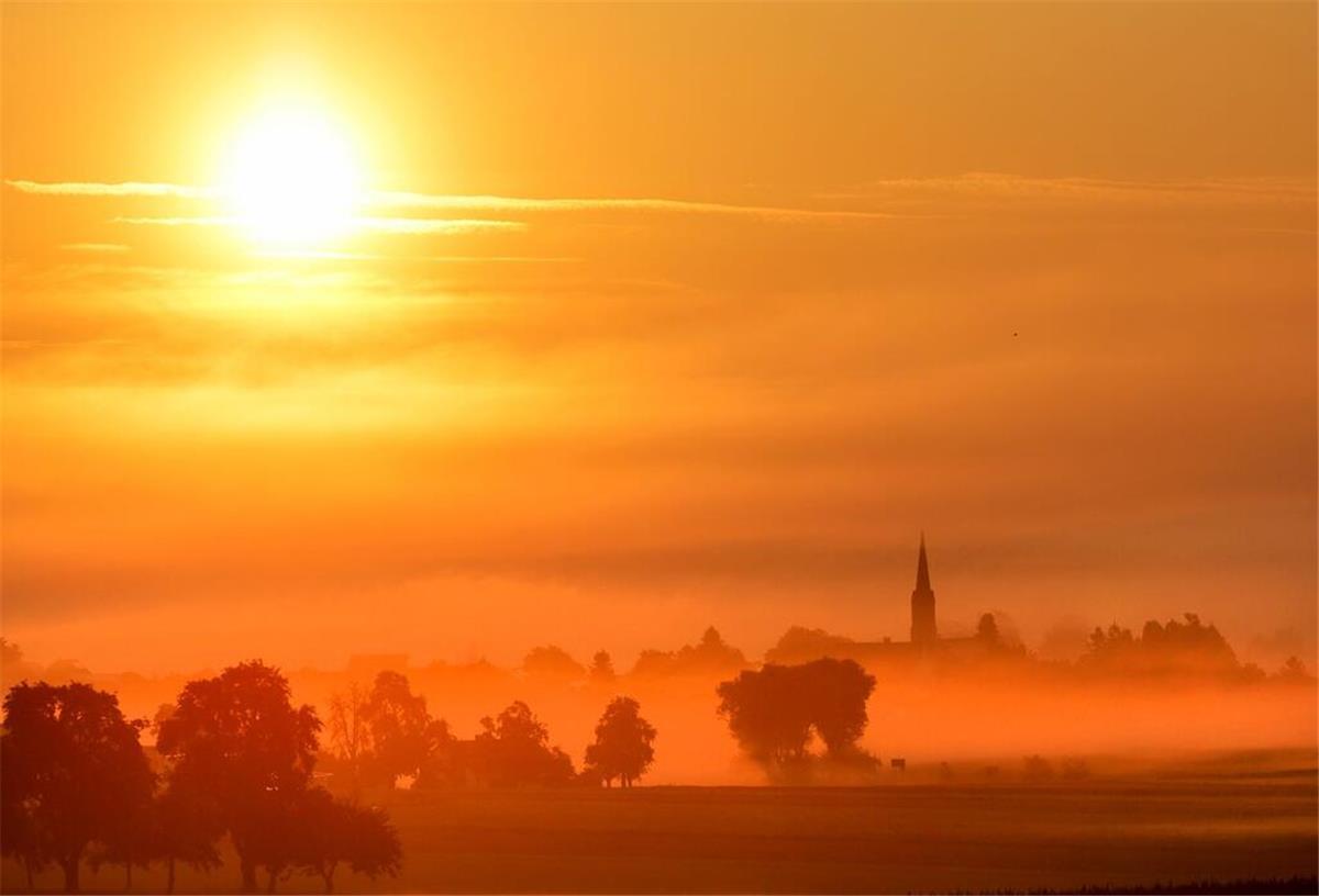Hinter dem Dorf Dieterskirch in Oberschwaben geht am Morgen die Sonne im Nebel auf.