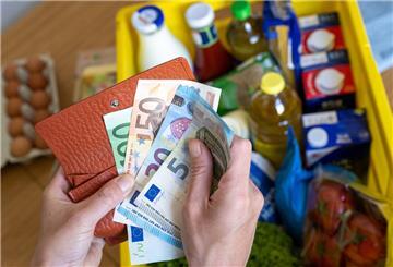 Zwei Hände über einem Lebensmittelkorb  halten eine Geldbörse und Geldscheine.
