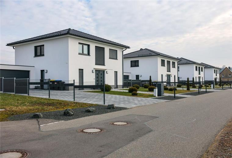 Vier uniforme Einfamilienhäuser stehen neu erbaut an einer Straße.