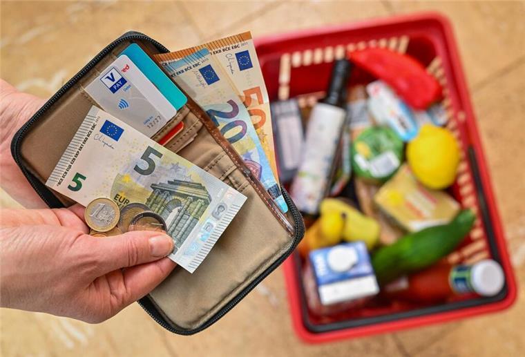 Eine Frau hält in ihrer Hand Geld vor einem vollen Einkaufskorb mit Lebensmitteln.