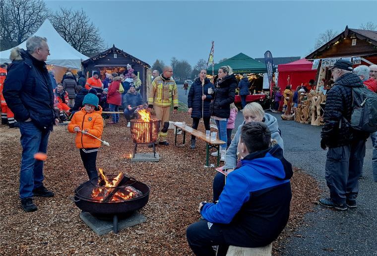 Menschen sitzen und stehen an Feuerschalen und Feuerkörben.
