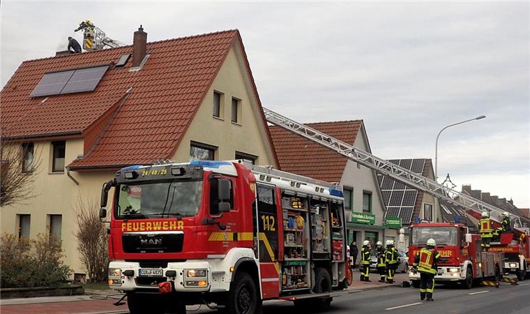 Schornsteinbrand in Langen: Straße drei Stunden gesperrt Zwei Feuerwehrwagen stehen in einer Straße. Per Drehleiter versucht ein Feuerwehrmann an einen Schornstein auf einem Haus zu kommen.