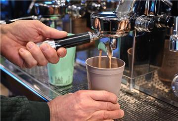 Ein Mitarbeiter eines Bio-Ladens bereitet einen Kaffee zu, der in einen Mehrwegbecher fließt.