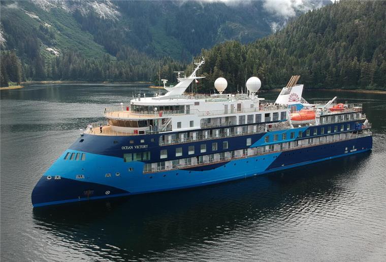 Kreuzfahrtschiff „Ocean Victory“ in Málaga festgesetzt Expeditionskreuzfahrtschiff „Ocean Victory“ fährt durch ruhige Gewässer, umgeben von bewaldeten Bergen.