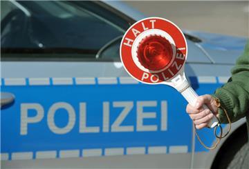 Eine Haltekelle wird von einem Polizisten vor einem Polizeifahrzeug.
