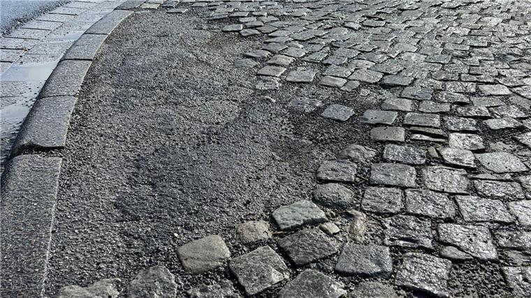 Pflastersteine und Fläche, die mit Bitumen geflickt wurde.