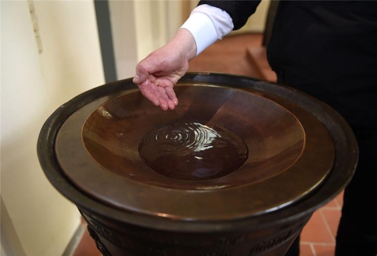 Oldenburger Kirche bietet spontane "Taufe to go" an Ein Mann steht mit seiner Hand am Taufbecken.