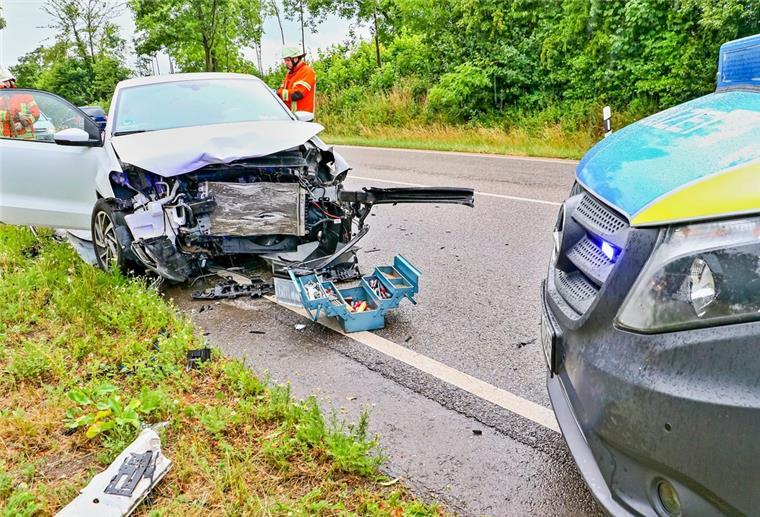 Ein verunfalltes Auto auf einer Landesstraße und ein nebenstehendes Polizeiauto.