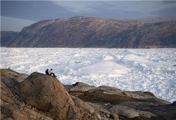 Zwei Studenten der New York University, die hier an einer Forschungsexkursion teilnehmen, sitzen auf einem Felsen mit Blick auf den Helheim-Gletscher.