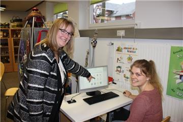 Die Verwaltungsangestellte und Datenschutzkoordinatorin bei der Gemeinde Stadland, Natascha Waidelich (stehend), und die Verwaltungsangestellte Merle Lienemann präsentieren den neuen Terminal in der Gemeindebücherei. Zusammen mit dem Personalausweis können wichtige persönliche Informationen abgerufen werden.