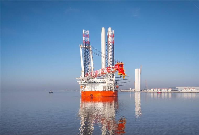„Wind Keeper“ verstärkt Cadelers Flotte für Windkraftinstallationen Offshore-Errichterschiff mit leuchtend orangefarbenem Rumpf und großem Kranaufsatz liegt bei klarem Himmel in ruhigem Hafenwasser; im Hintergrund sind Hafenanlagen und Windkraftkomponenten zu sehen.