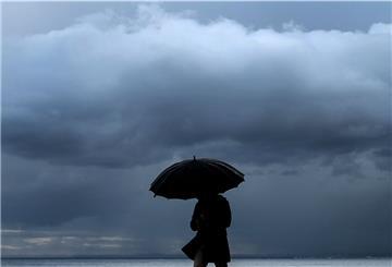 Ein Mann hält einen Regenschirm, während er am Meer entlang spazieren geht.