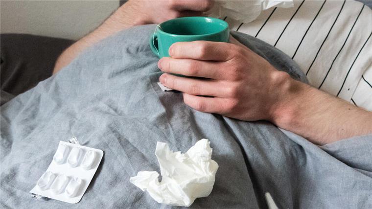 Die Grippewelle hat Bremerhaven fest im Griff Ein Mann liegt mit Taschentüchern, Teetasse, Nasenspray und Tabletten im Bett (gestellte Szene).