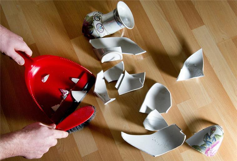 Ein Mann kehrt eine kaputte Vase mit einem Handfeger auf.