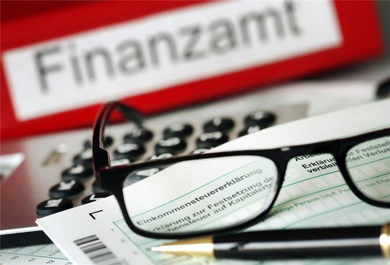  Auf einem Vordruck für die Steuererklärung liegen vor dem Aktenordner mit dem Aufdruck «Finanzamt» ein Stift und eine Brille. 