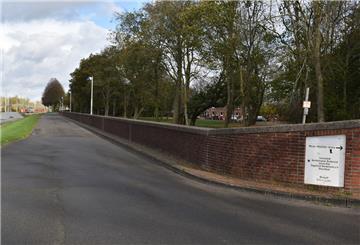 Neben einer leeren Straße ist links ein Grünstreifen und rechts eine Steinmauer zu sehen.