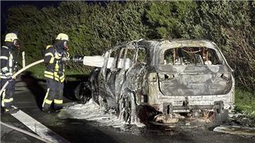 Zwei Feuerwehrleute stehen neben einem ausgebrannten Auto und besprühen es mit Löschschaum.