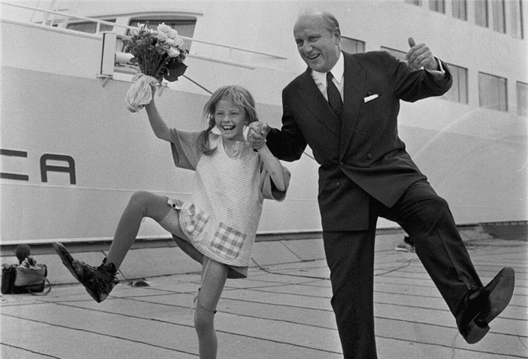 Pippi taufte Bremerhavener Fähre: Das bewegte Leben der Fähre „Stena Danica“ Schauspielerin Inger Nilsson als Pippi Langstrumpf tanzt mit Blumenstrauß in der Hand lachend neben Reeder Sten A. Olsson vor der „Stena Danica“, Sommer 1969.