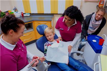 Dr. Katja Baake (links) kitzelt Bens Finger mit einem „Kitzelbagger“. Das dient der Entspannung des kleinen Patienten. Es assistiert Helferin Noura Abou-Chlaih. Jenna Kück (rechts), Bens Mutter, ist auch dabei.  