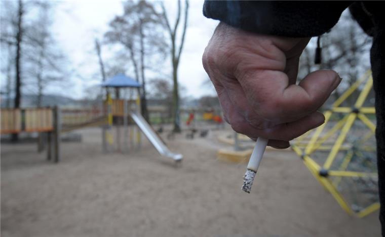 Ärzteverband für Rauchverbote auf Spiel- und Sportplätzen Ein Mann hält auf einem Spielplatz eine Zigarette in der Hand.