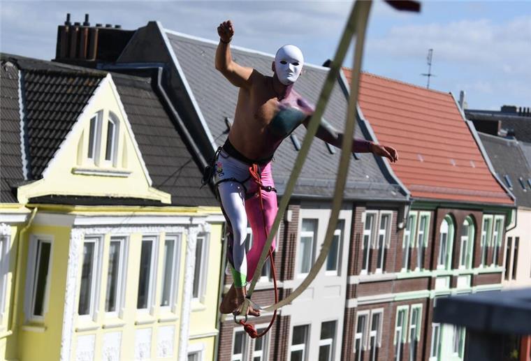 Bremerhaven: Künstler können sich für Artspace-Festival bewerben Ein Akrobat jongliert hoch über einer Straße zwischen Altbauten auf einem Seil