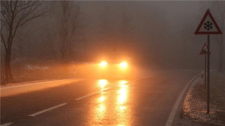 Ein Auto fährt bei Glatteis und Nebel über eine Straße.