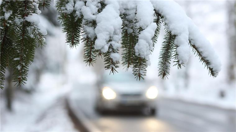 Ein Auto fährt hinter einem schneebedeckten Zweig über die Straße.