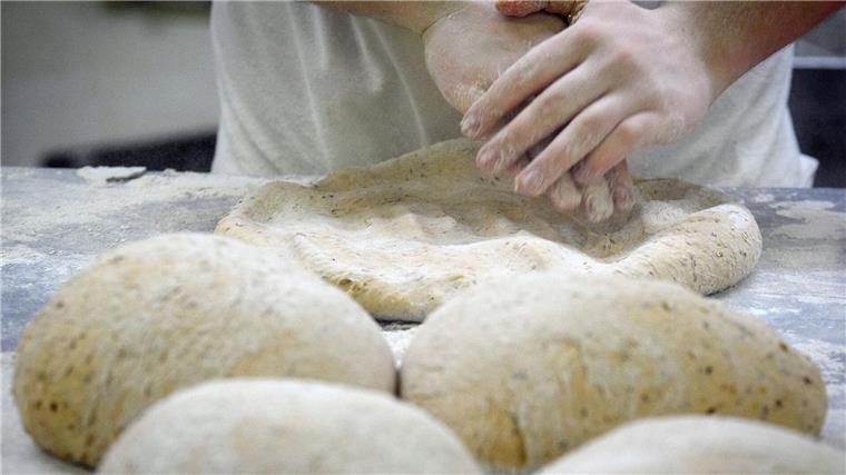 Zwei Bäckereigroßhändler fusionieren zu größtem Anbieter Ein Bäcker formt in der Backstube auf einer mit Mehl bestäubten Arbeitsplatte den Teig.