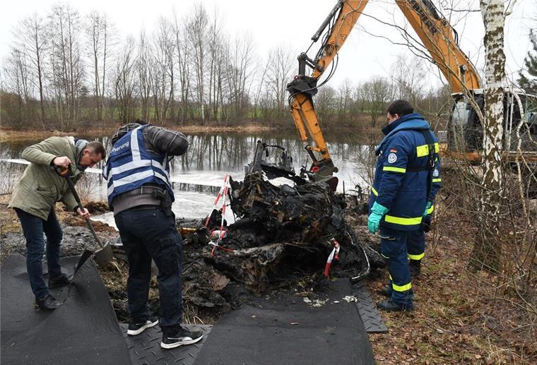 Bagger birgt Pkw-Überreste aus Lunestedter See Drei Männer untersuchen die Überreste eines Autos an einem See. Daneben steht ein Bagger.