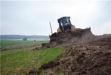 Ein Bagger schält den Mutterboden vom Deich ab. Anschließend wird er mit schwerem Kleiboden erhöht. Am Ende wird der Mutterboden wieder breitgefahren, damit das Gras schneller anwächst.