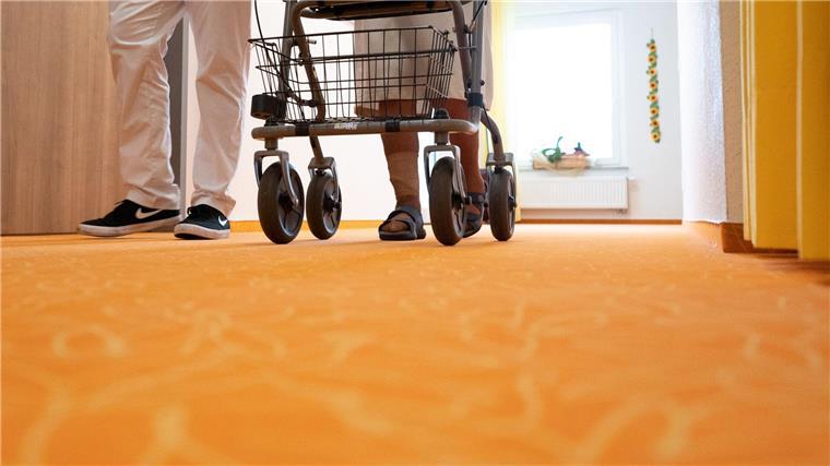 Pflegerat: Einstiegsgehalt 4000 Euro für Pflegefachkräfte Ein Betreuer geht in einem Pflegeheim mit einer Bewohnerin über den Flur.
