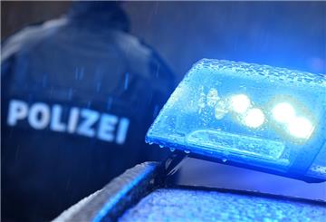 Ein Polizist steht im Regen vor einem Streifenwagen dessen Blaulicht aktiviert ist.